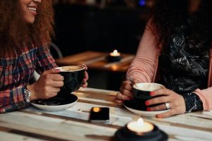 Photo of two women sitting at a table drinking from mugs and smiling. This photo represents how you can control your holiday anxiety in Gallatin, TN. Learn tips on how to be less anxious here.
