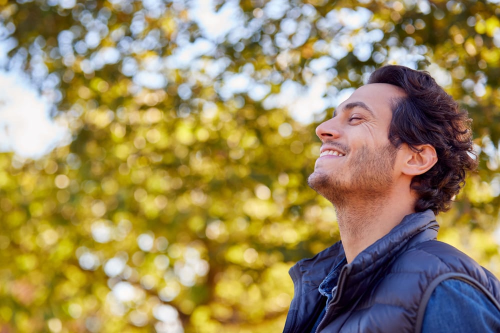 man smiling with chin up with fall leaves in background