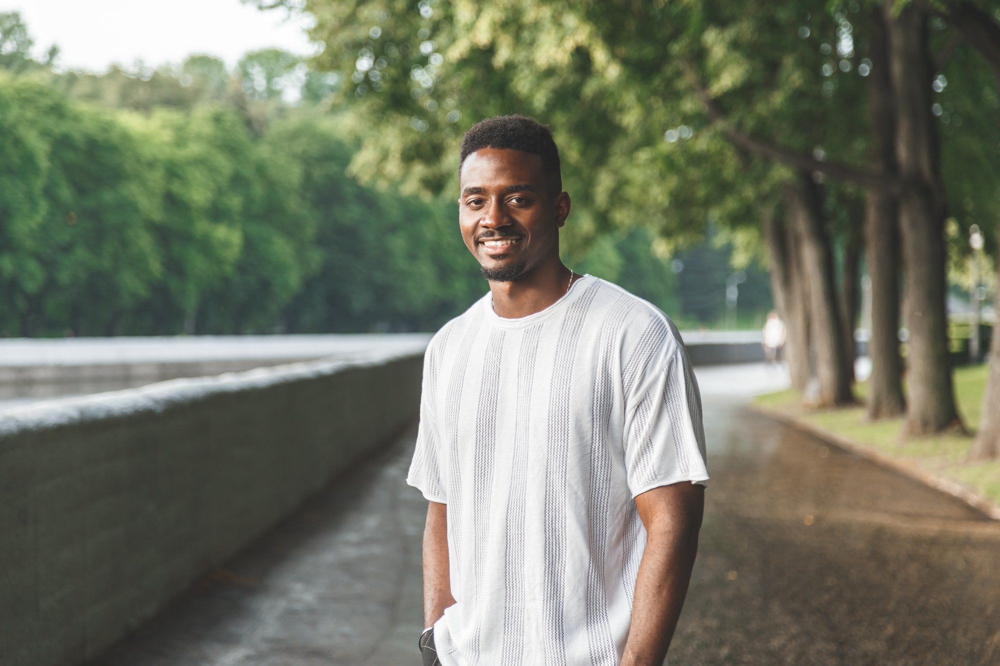 TN Mental Wellness young man smiling with hands in pockets outside on a park trail with trees in the background