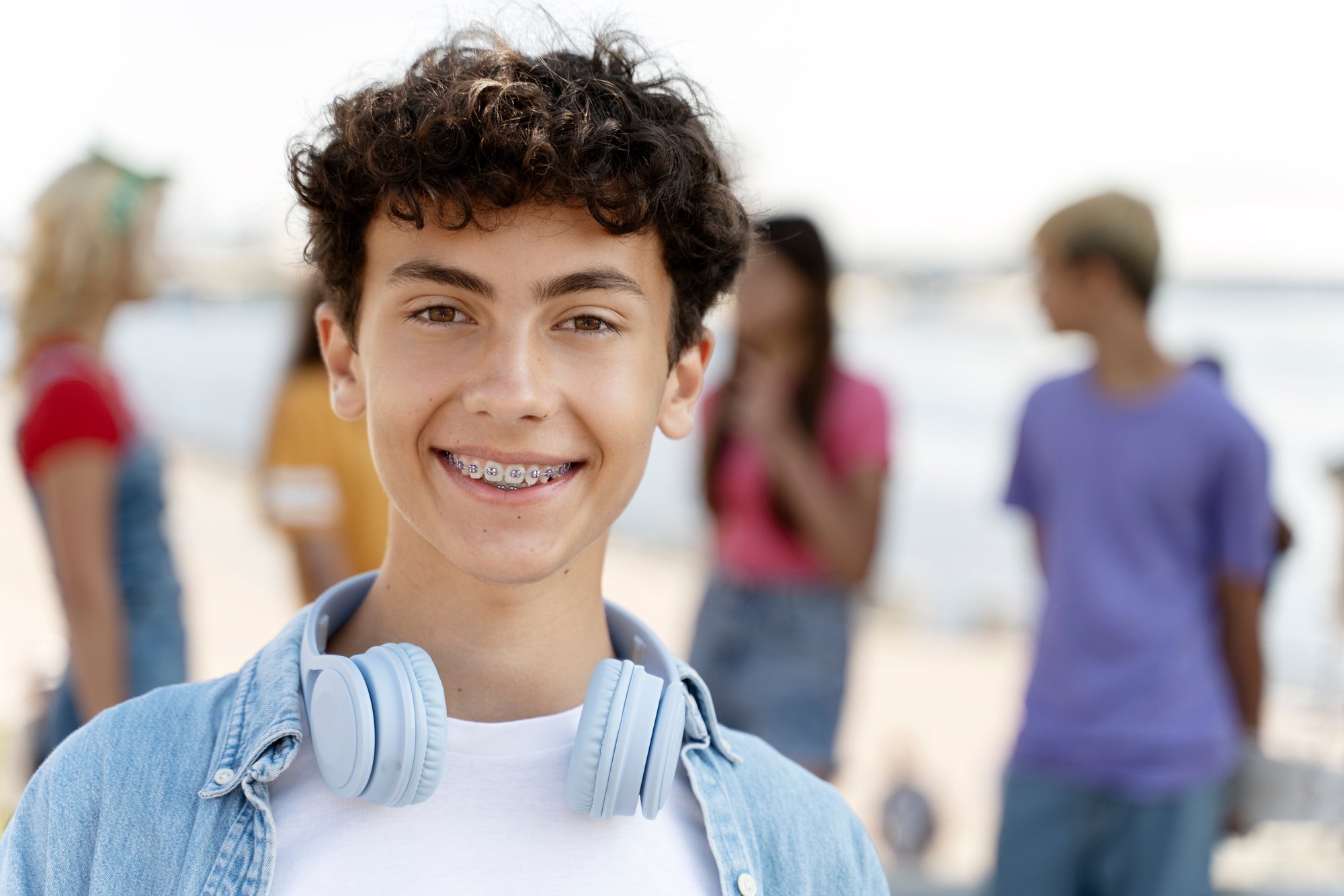 TN-Mental-Wellness-Teen-boy-smiling-with-braces-and-headphones-around-his-neck-with-people-in-background