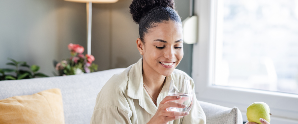 a woman sitting on couch while holding an apple and a glass of water 